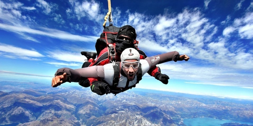 Customer doing a thumbs up while tandem skydiving above Queenstown with NZONE